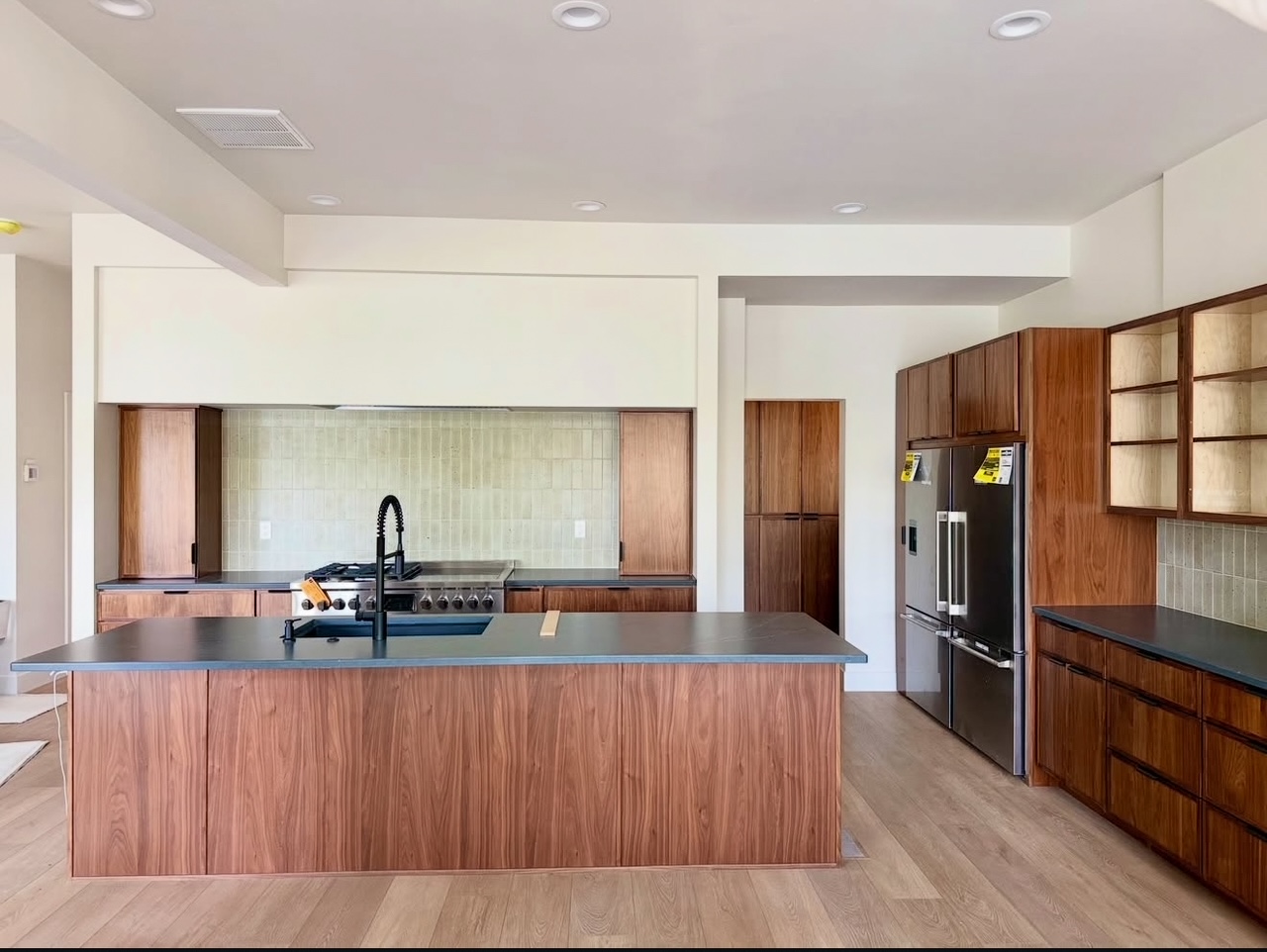 Modern kitchen with walnut island, dark countertops, tile backsplash, stainless appliances, and recessed lighting.