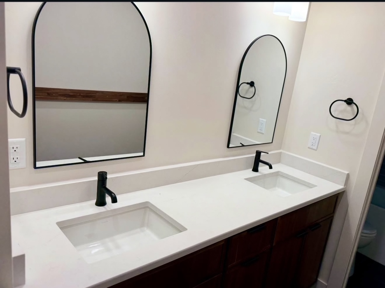 Bathroom double vanity with white countertop, undermount sinks, matte black faucets, and arched mirrors.