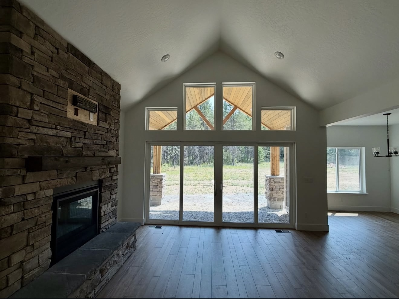 Spacious living room with vaulted ceiling, stone fireplace, hardwood flooring, and large glass patio doors.