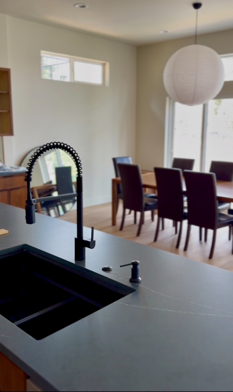 Kitchen island with black faucet and undermount sink looking toward dining table and paper pendant light.