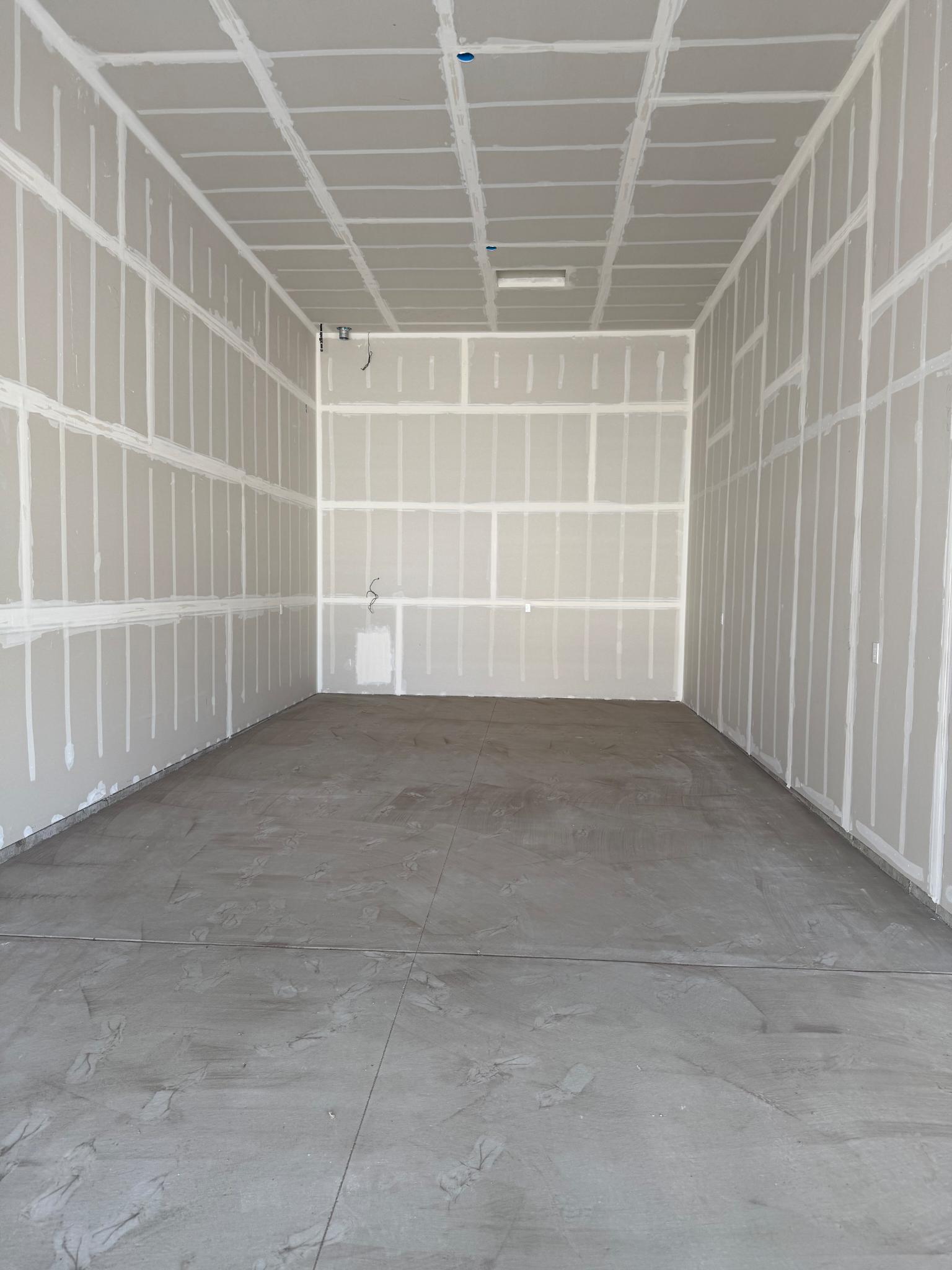 Empty interior room with hung drywall panels on walls and ceiling and white joint compound on the seams.