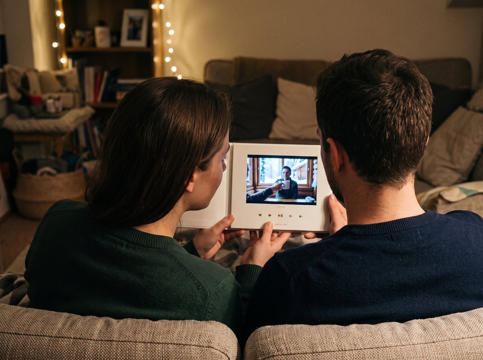 Couple on a sofa under string lights watching a group video on an open Tribute Video Book