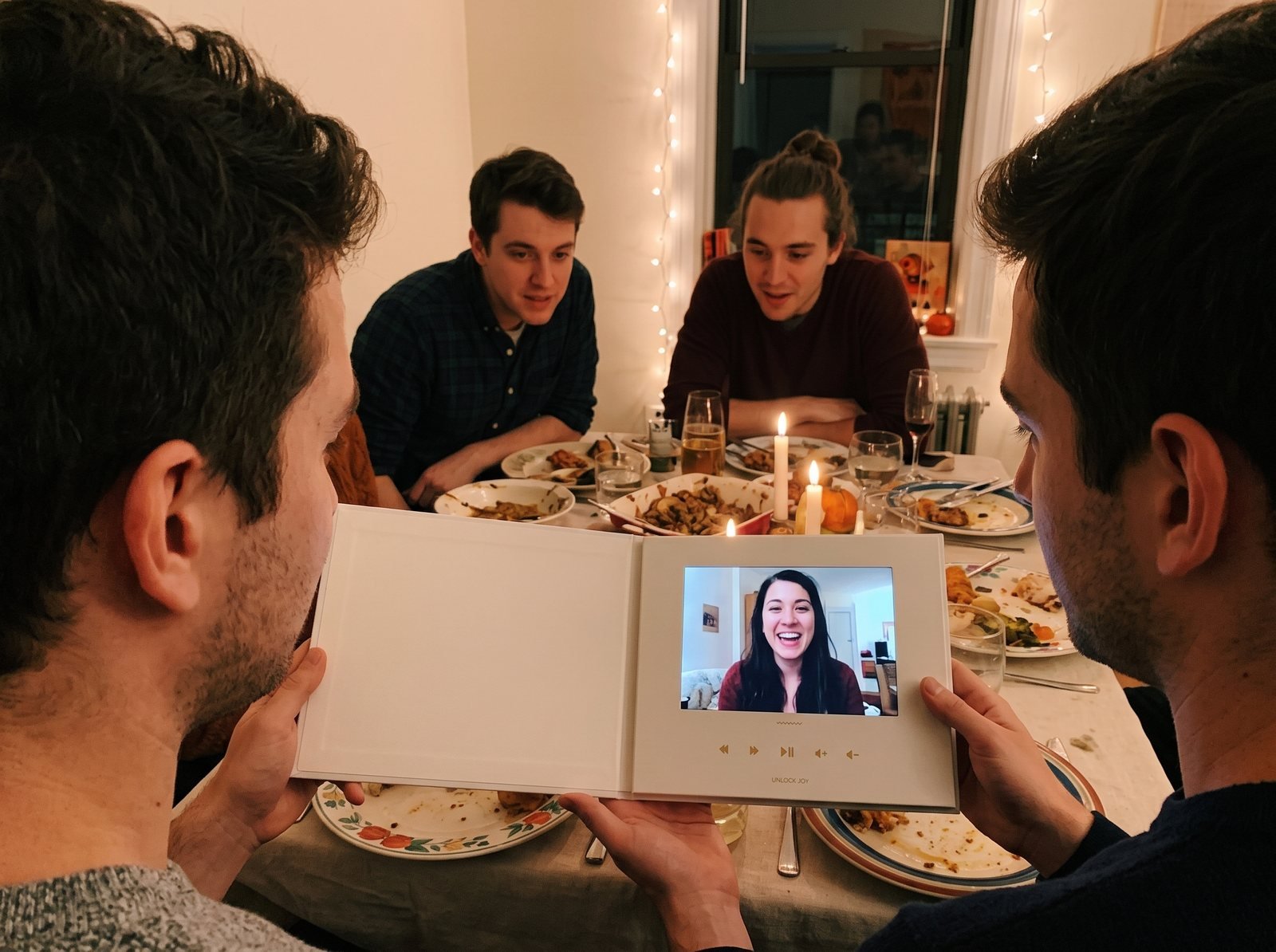Friends at a cozy Friendsgiving dinner watching a group video on an open Tribute Video Book